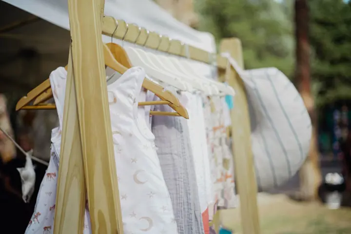 Roupas de criança penduradas em cabides de madeira, numa arara ao ar livre.