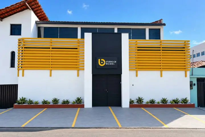 Fachada branca de dois andares, com ripas amarelas dos dois lados, porta preta e o letreiro Studio CB Model num painel preto sobre a porta.