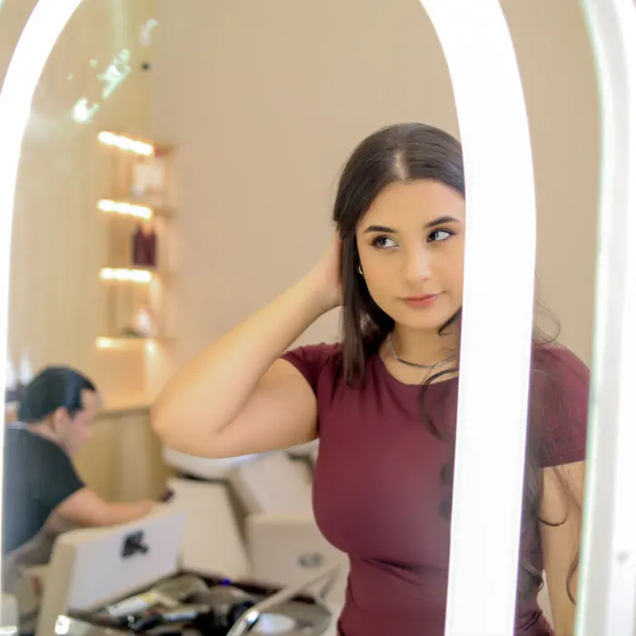 Modelo de cabelo escovado, de pe diante do espelho iluminado de um salao